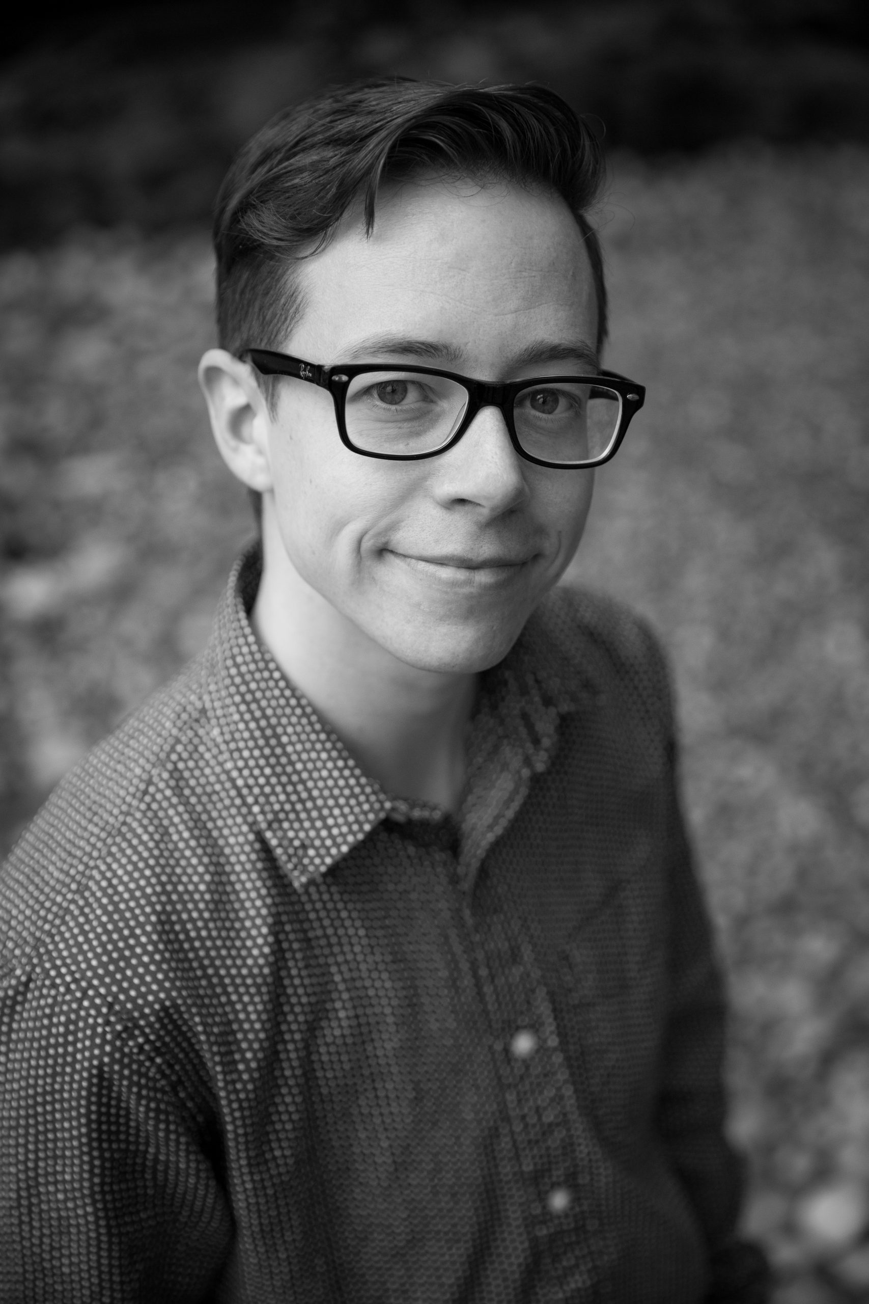 Portrait of a person with short hair and dark-rimmed glasses, smiling with mouth closed.