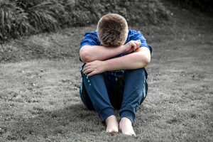 Boy sitting on ground, knees to chet and head in arms