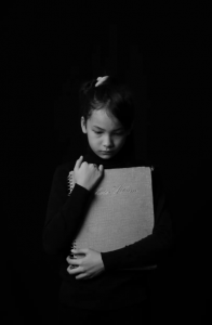 Black and white photo of girl looking down, clutching book to her chest
