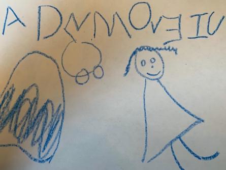 Child's writing has letter-like symbols in different colors and a face with two eyes and a smiling mouth.