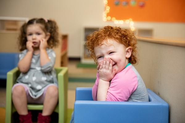 Two children sit in chairs in the classroom and respond to their teacher.