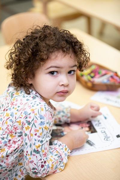 A child uses a crayon to draw a picture next to a photograph of her family