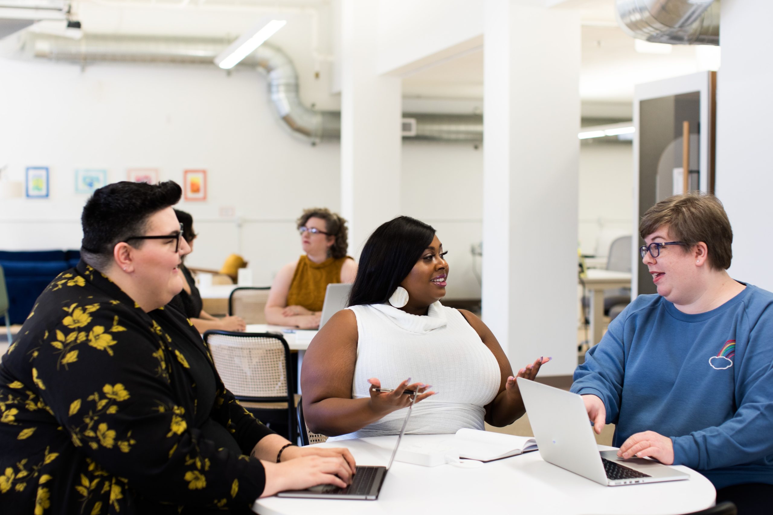 Three women sitting around a table with laptops.