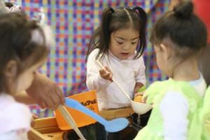 Three children playing in the water table with ladles and spoons.