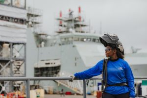 student standing in front of a ship at the shipyard