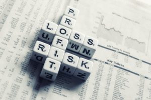 Dice with letters sitting on a newspaper. The dice words connect crossword style and read profit, loss, risk.
