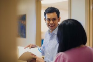 Two individuals, one holding papers and smiling, implying a positive interaction or collaboration.