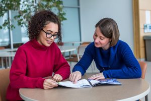 student and faculty engaged in positive conversation while looking at text book