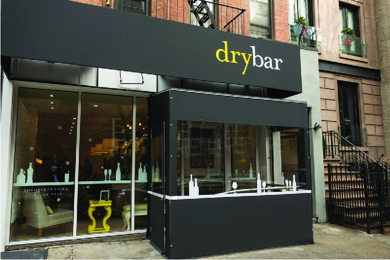 A glass window store front with a black canopy as seen from the sidewalk.