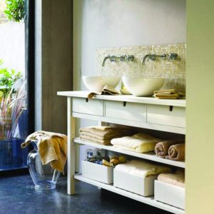 A bathroom vanity with two sinks, and towels folded on shelves underneath.