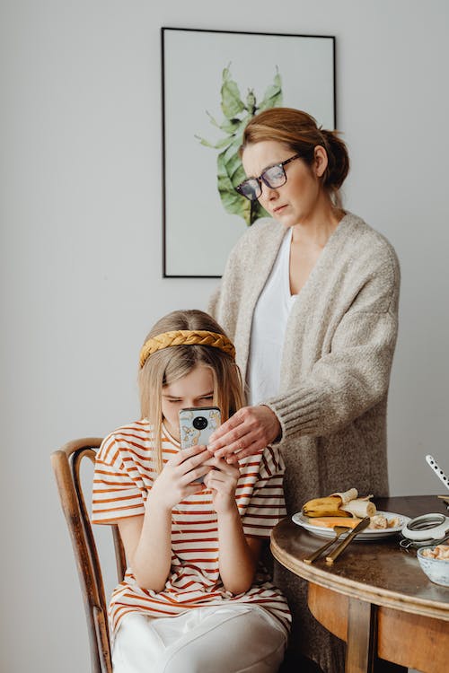 Mother looks over daughter's shoulder at her phone.