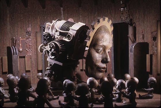 Giant robotic face looking down on sitting robotic children