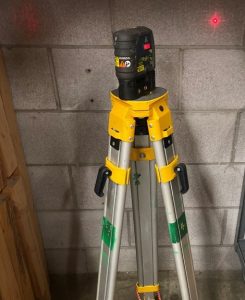 A laser situated on a tripod. The laser beam reflects off a nearby wall.