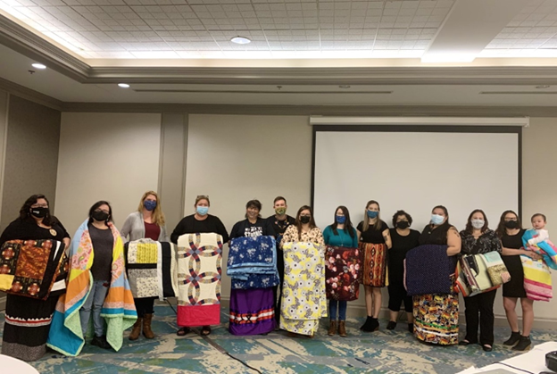 13 students wearing covid facemasks holding or draping blankets arounf their shoulders.