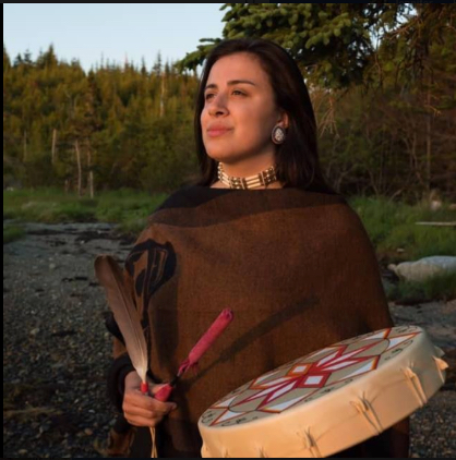 Photograph of Mi'kmaw artist, Melanie Hardy, looking away from camera. Melanie is holding a Pepkwejete’maqn, a Mi'kmaq drum, and a feather.