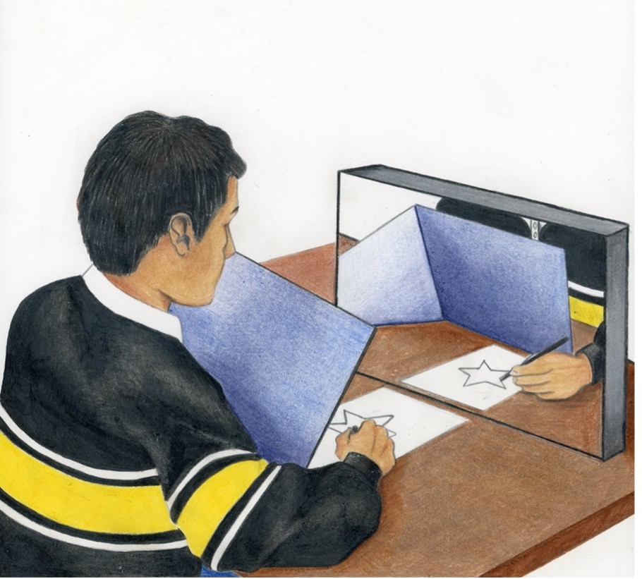 A person is sitting at a desk with a mirror propped up in front of them. In front of the mirror on the desk is a piece of paper with an image of the star. The person has a blue piece of board in between them and the paper, so they cannot see the physical paper, only the reflection of the paper in the mirror. The person is holding a pencil and attempting to trace the outline of the star by looking at the reflection in the mirror.