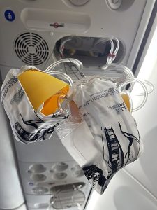 Airplane oxygen masks hanging down from the overhead compartment inside a passenger aircraft. The yellow masks with attached clear plastic bags and tubing have deployed, ready for use.